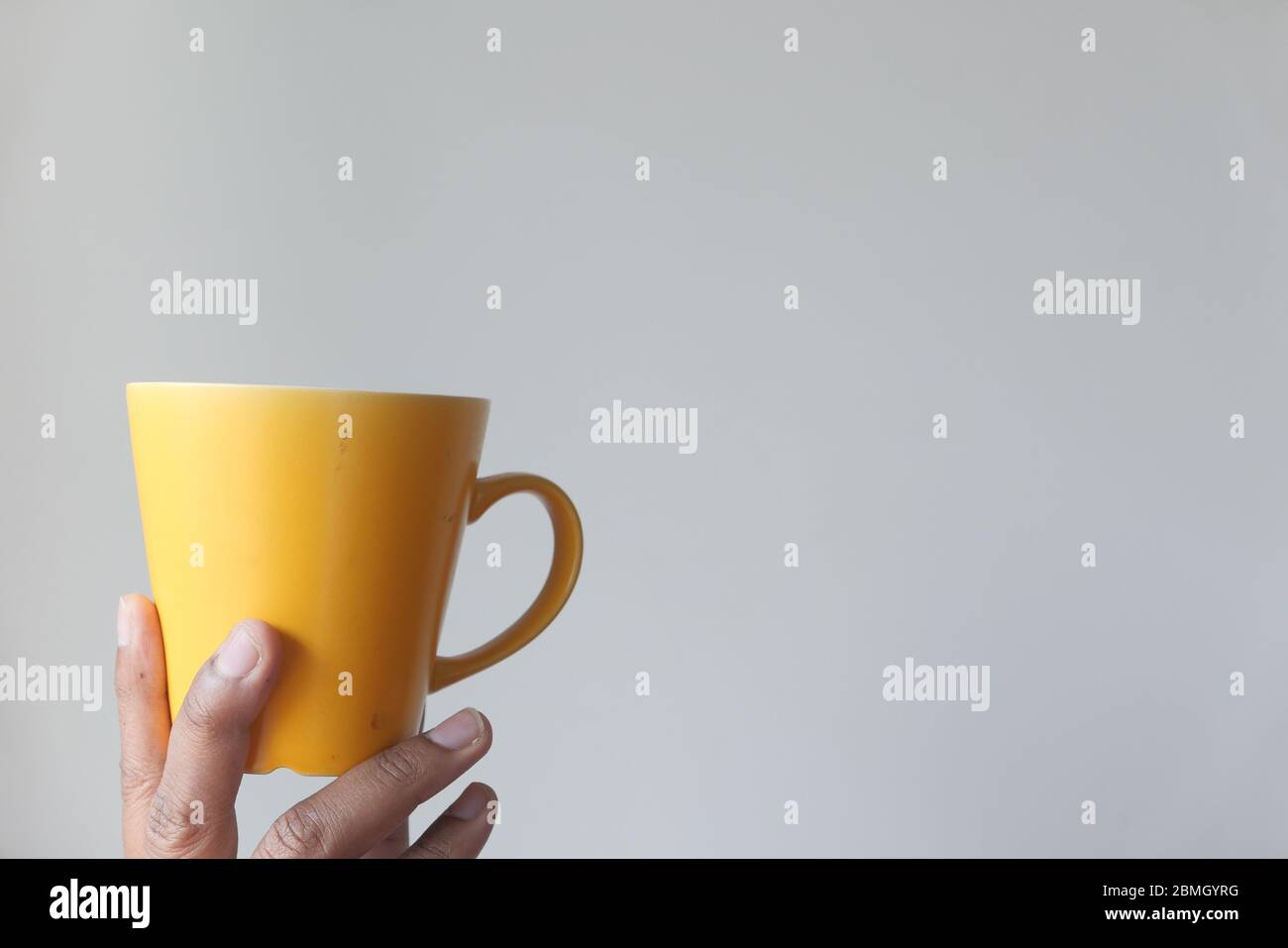 Hand hält gelben Becher an einer Wand. Stockfoto