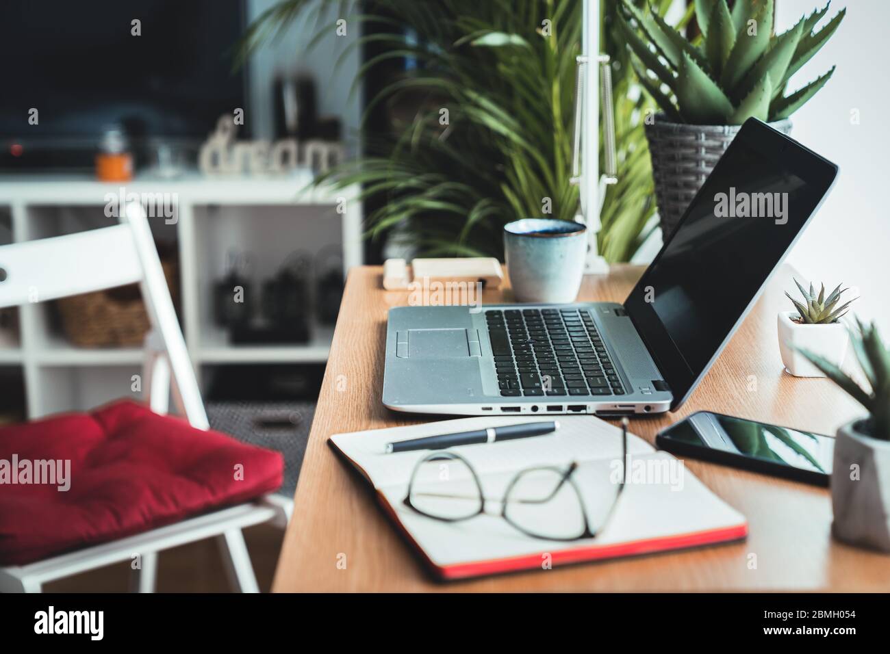 Nahaufnahme eines Holzschreibtisches mit Laptop, Planer, Handy und Brille auf dem Arbeitstisch. Arbeiten von zu Hause Konzept mit Fensterlicht Stockfoto