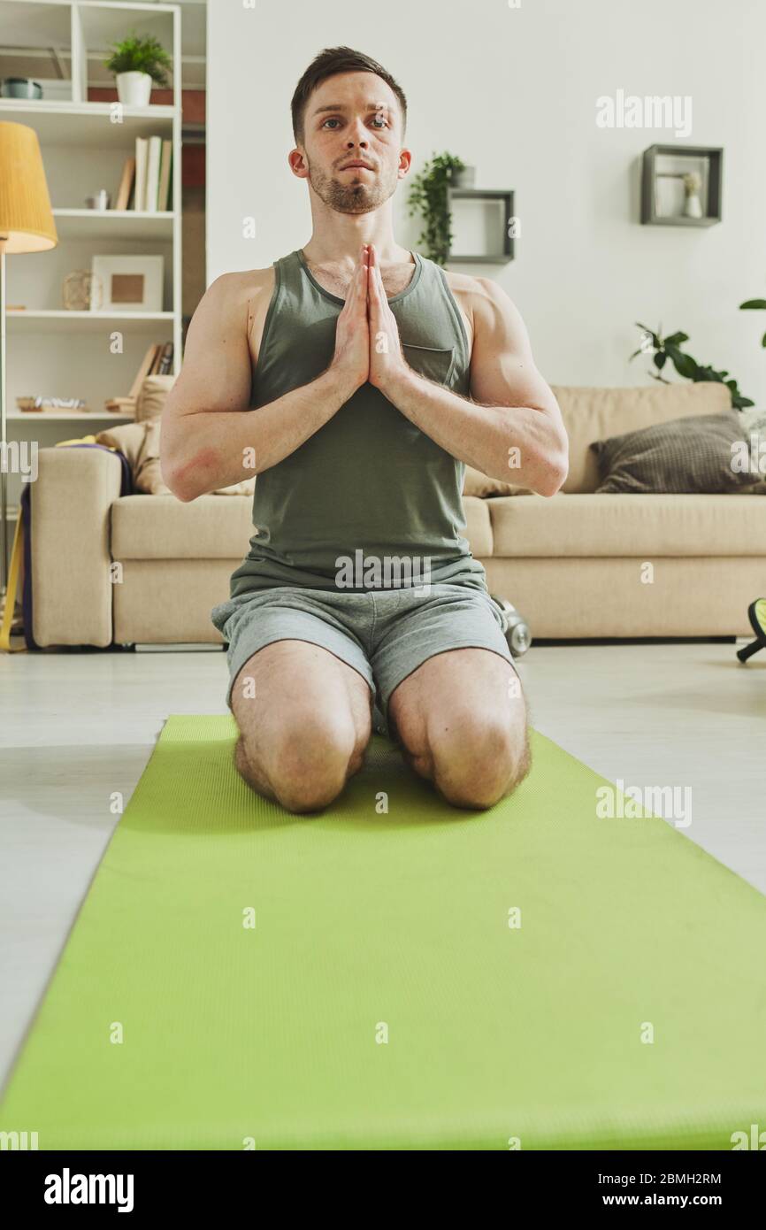 Entspannter Mann in der aktiven Ohr mit seinen Händen zusammen nahe an der Brust stehend auf den Knien während einer der Yoga-Übungen Stockfoto