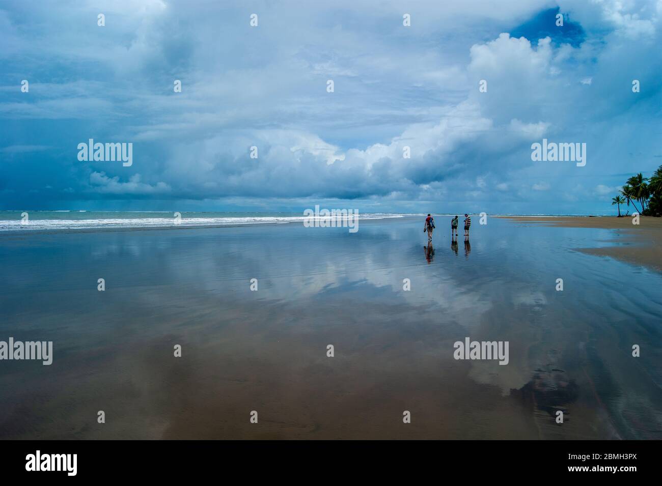 Drei Spaziergänge entlang eines Strandes in einem Sturm reflektierend Stockfoto