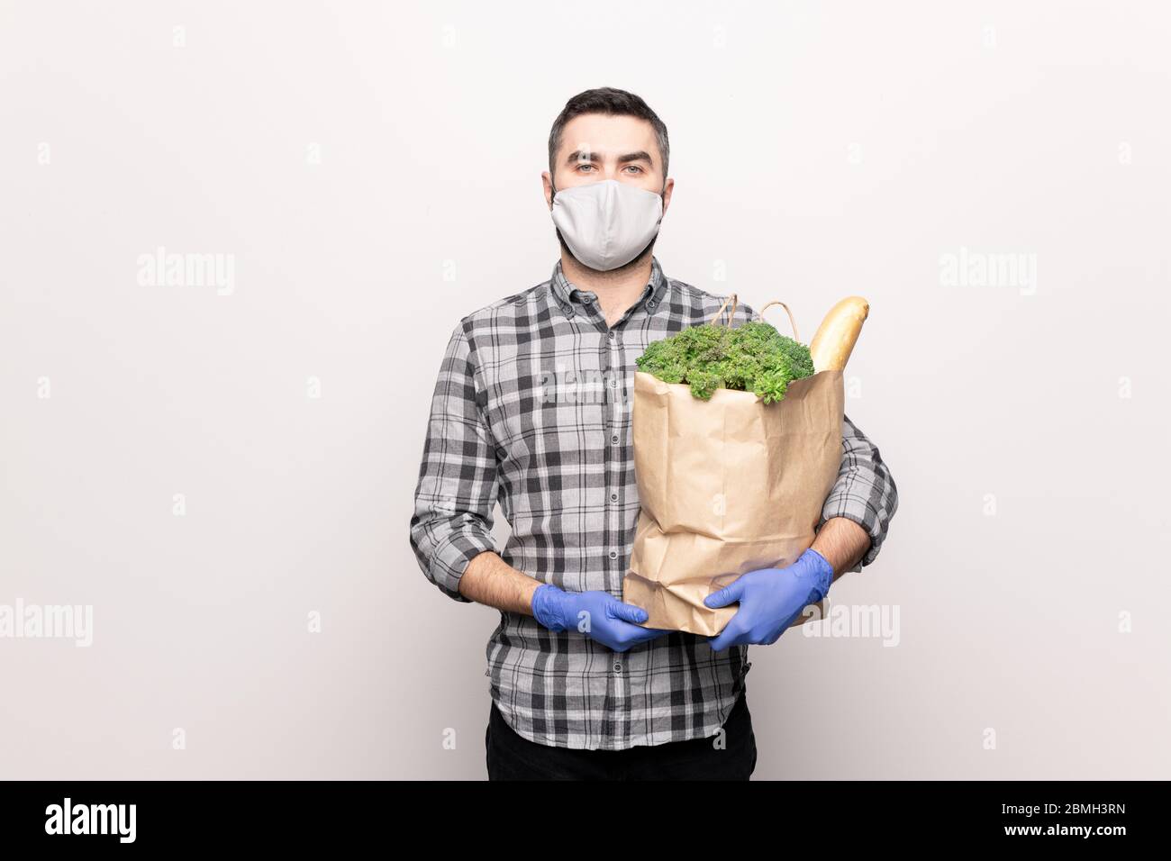 Ernst junger Mann in Schutzmaske und Handschuhe halten Papierpaket mit frischen Lebensmitteln, während sie zu Ihnen nach Hause liefern Stockfoto