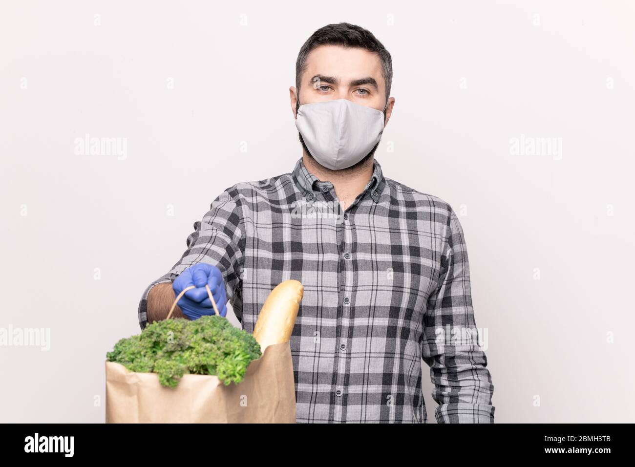 Junge Kurier in lässigen Hemd und Schutzhandschuhe und Maske vorbei Sie Papiertüte mit frischen Lebensmitteln aus dem Supermarkt Stockfoto