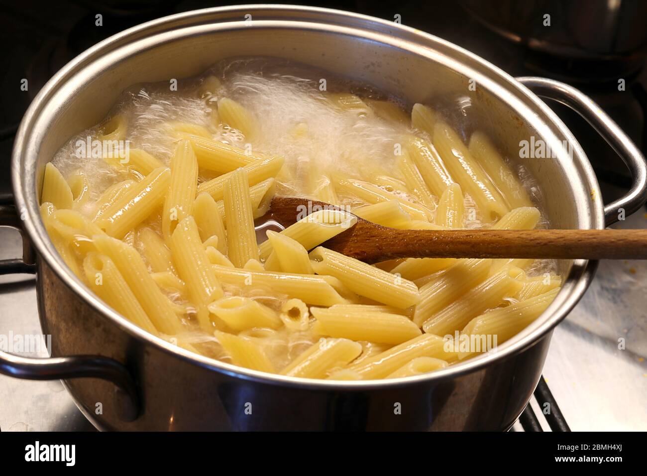 Topf mit kochendem Wasser und die italienische Pasta während des Kochens und einen Holzlöffel zum Mischen Stockfotografie