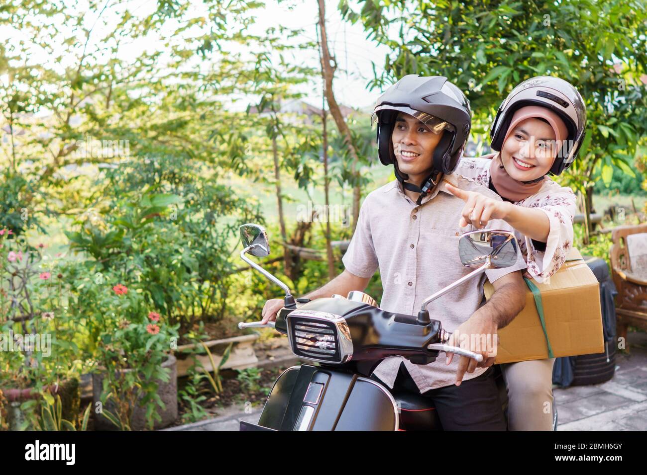 Fröhlicher muslim, der mit dem Motorroller auf eid mubarak mit Koffer unterwegs ist Stockfoto