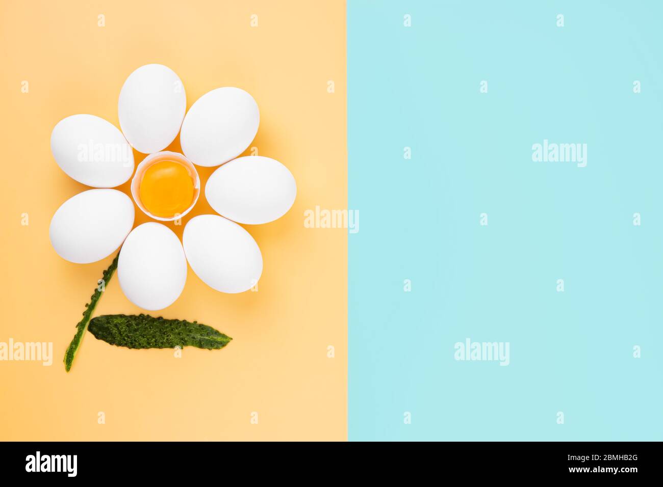 Weiße Hühnereier, die in einer Kamillenblütenform angeordnet sind, mit einer Eierschale in der Mitte mit Eigelb und Gurkenschälen als Stiel Stockfoto