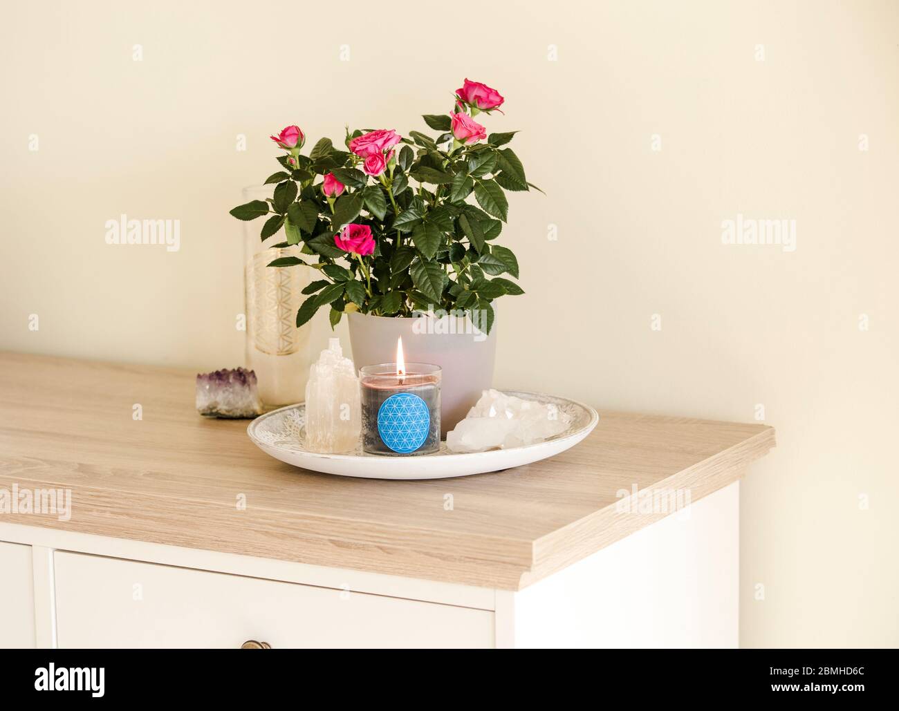 Brennende Glaskerze mit selbstgemachtem Schild, das das Symbol Blume des Lebens im Inneren mit Halbedelstein-Geoden zeigt. Spirituelle Symbole zu Hause. Stockfoto