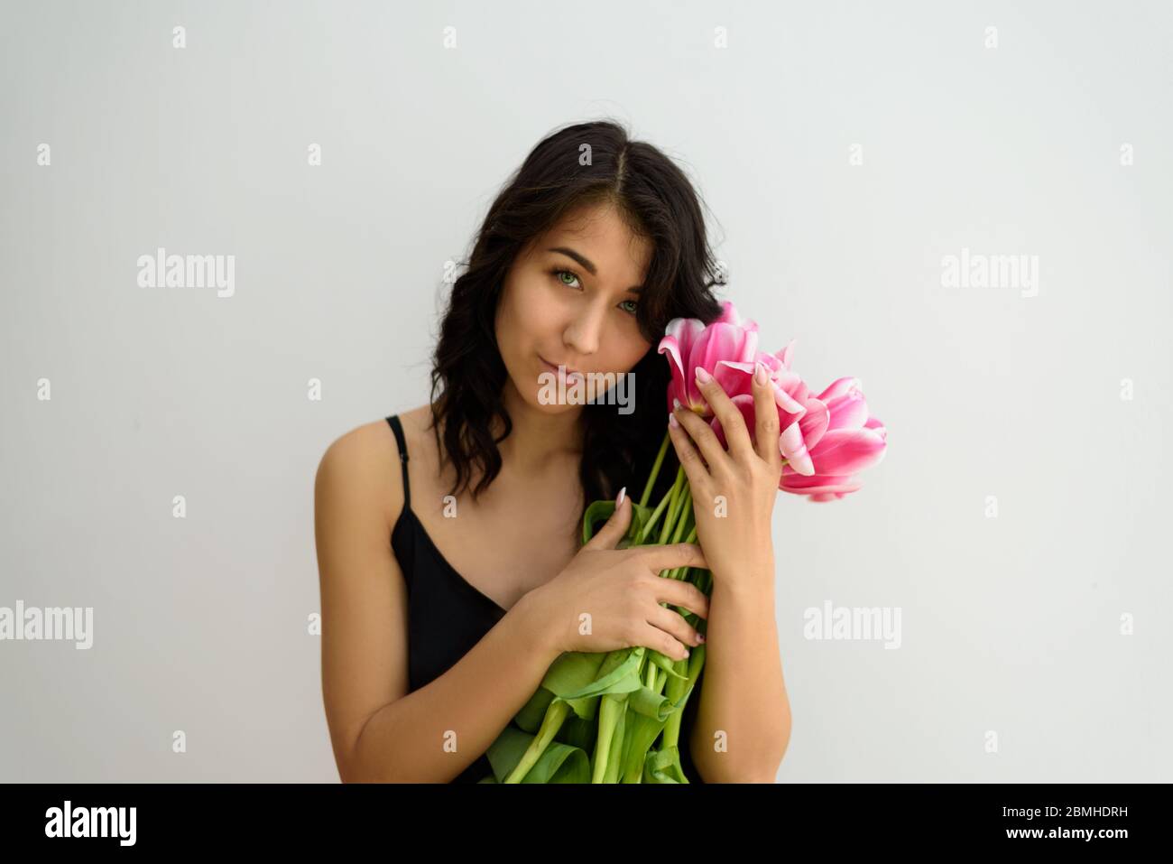 Ein Porträt von charmanten dunkelhaarigen jungen Frau mit vielen schönen rosa Tulpen auf dem weißen Hintergrund. Stockfoto