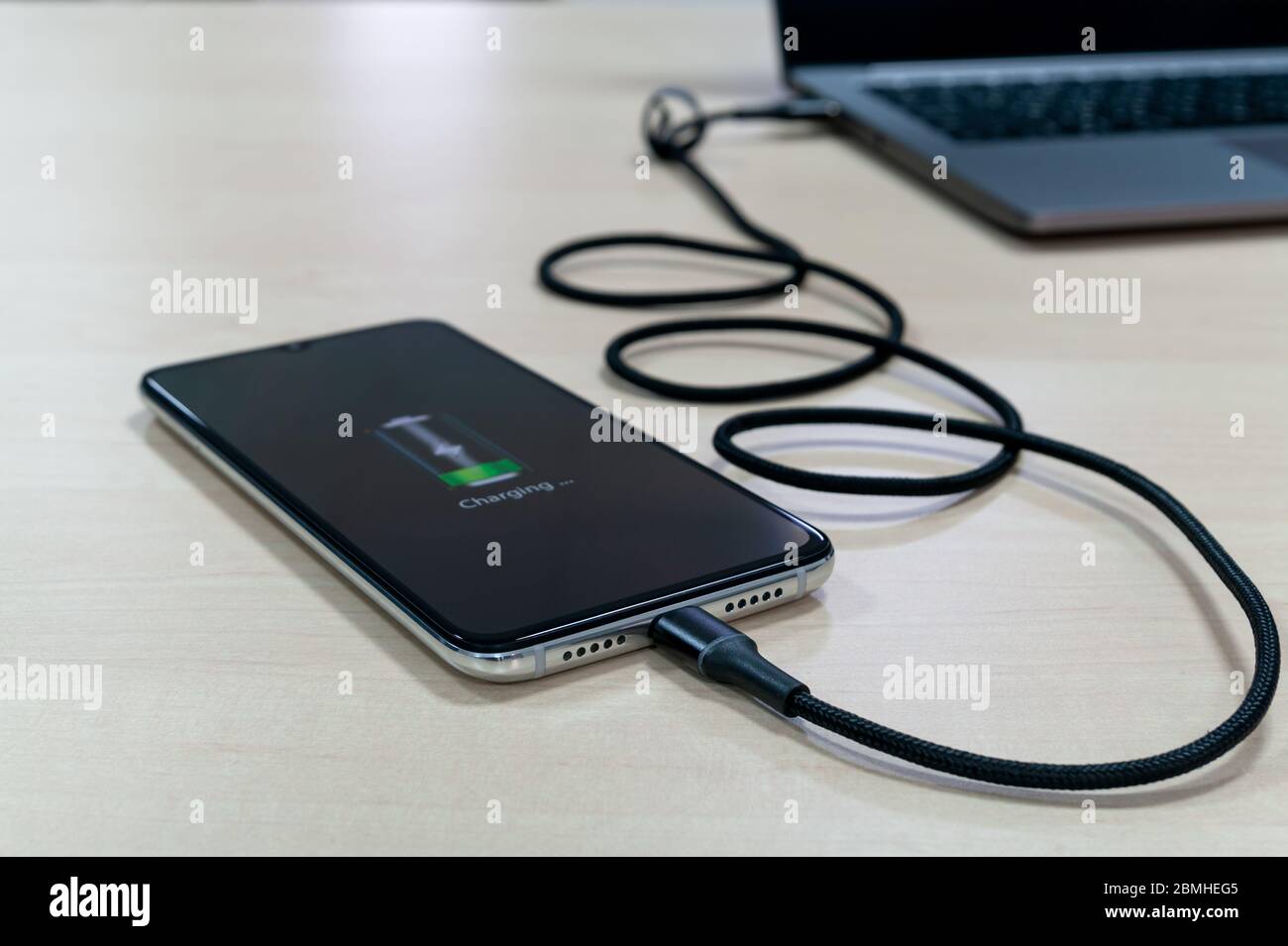 Moderne Smartphones laden vom Laptop auf einen hellen Holztisch. Modernes Technologiekonzept. Selektiver Fokus Stockfoto