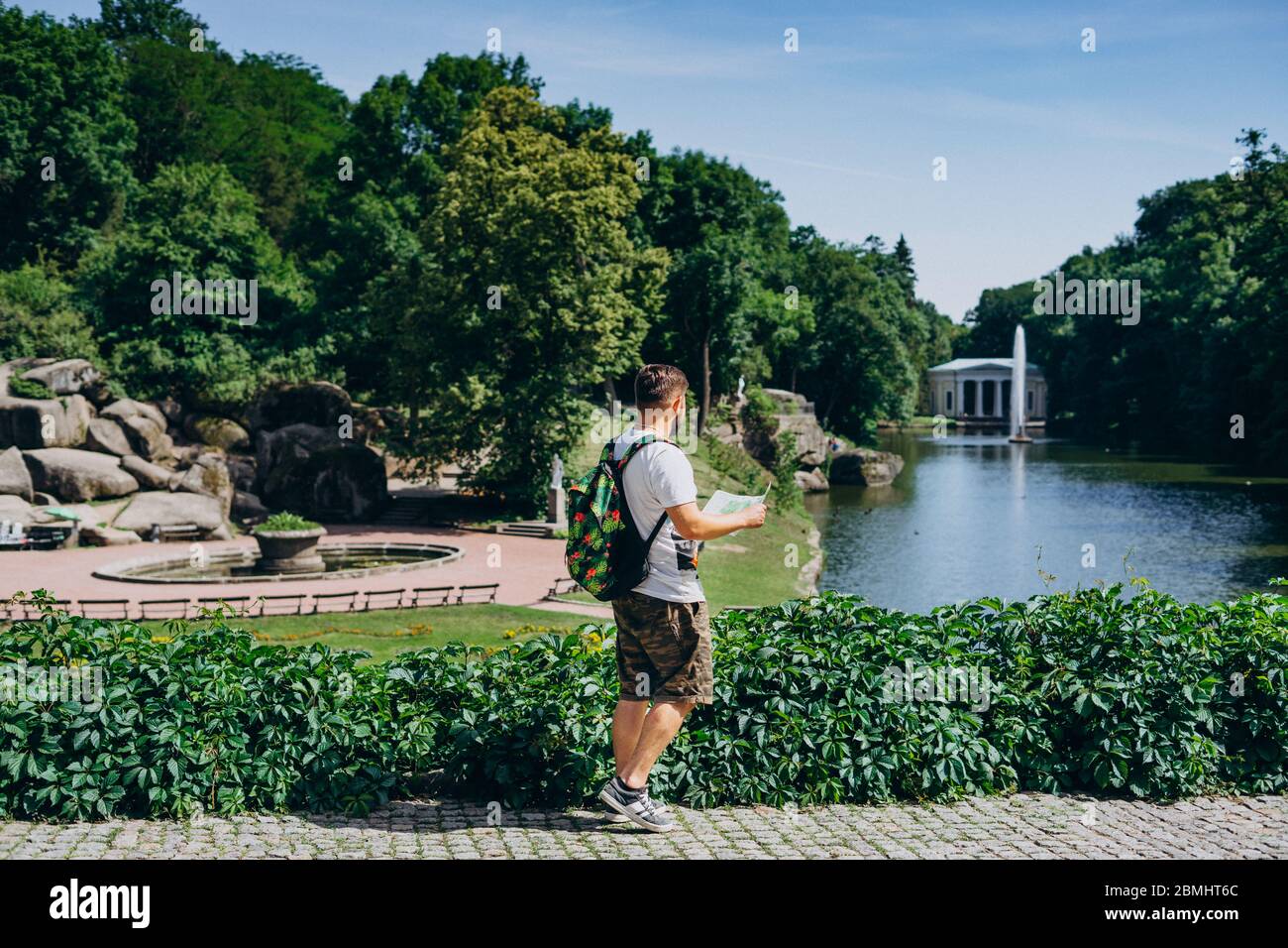 Sofia Park, Ukraine. Mann mit Rucksack und Touristenkarte im Sommer in einem Landschaftspark. Typ in einem T-Shirt mit einer Touristenkarte auf dem Hintergrund von Th Stockfoto
