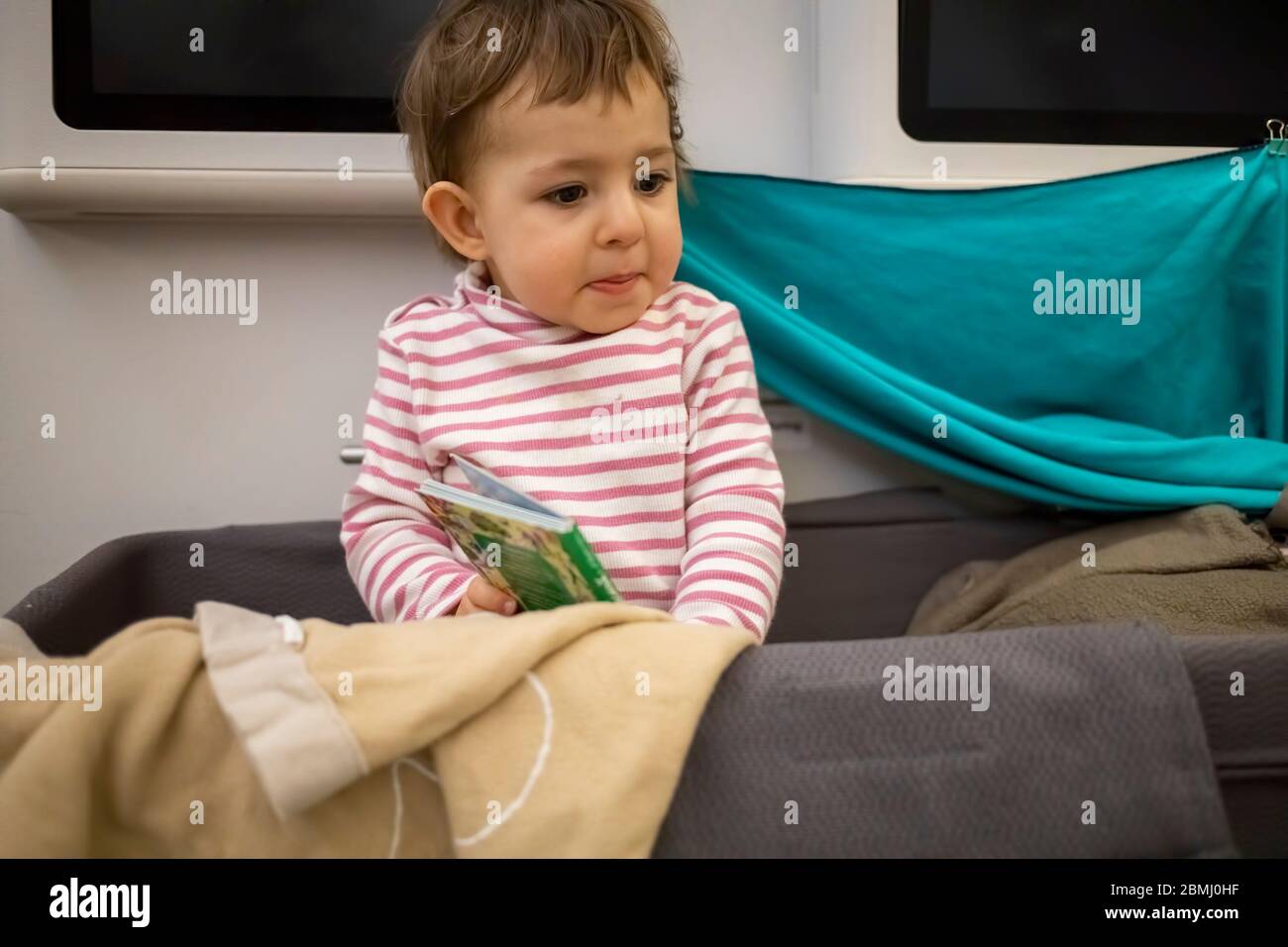 Kleines niedliches Kleinkind, das in Babyschulterwagen eines Flugzeugs sitzt und mit einem erschrockenden Blick herum schaut. Stockfoto