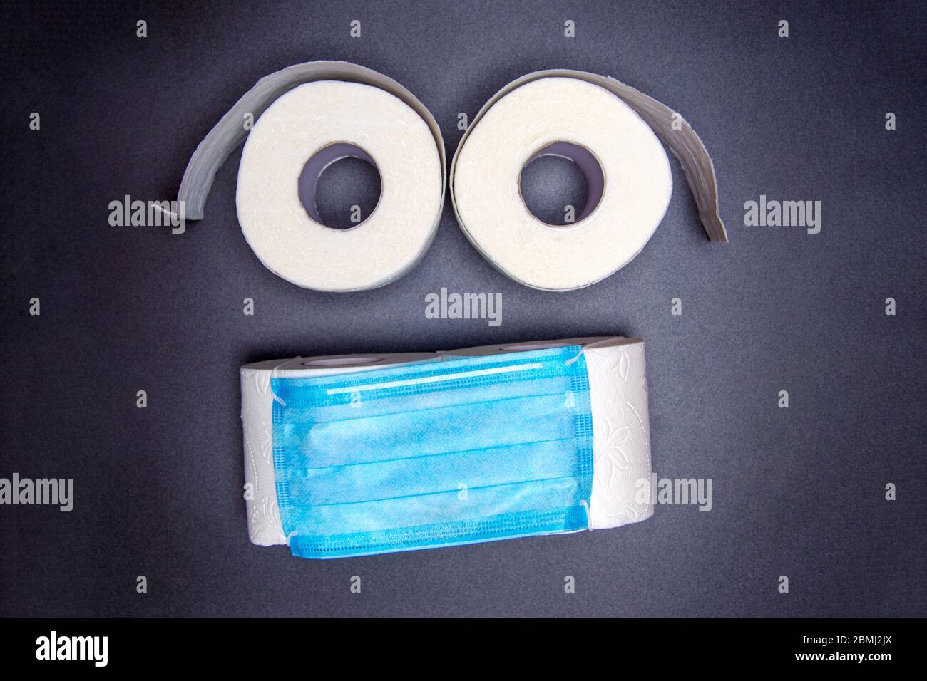 toilettenpapier Rollen sind in Form eines Emoticons mit einer blauen medizinischen Gesichtsmaske ausgelegt. Auf schwarzem Hintergrund. Virus Ausbruch Konzept. Coronavirus n Stockfoto