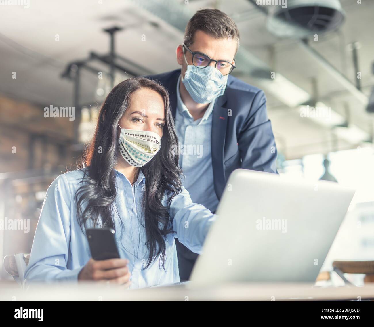Gut aussehende weibliche und männliche Kollegen sehen zusammen auf den Computerbildschirm, tragen Gesichtsmasken. Stockfoto