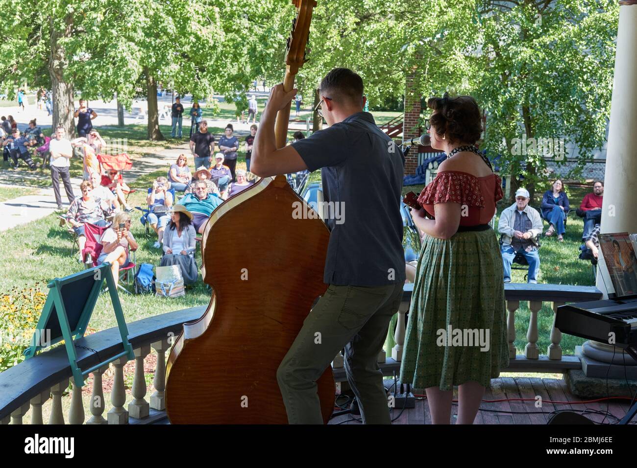 Attraktive junge Retro-Paar singen und spielen Kontrabass und Ukulele zu einer Menge im Freien bei einem Sommer Veranda Konzert-Event in einer historischen Residenz Stockfoto