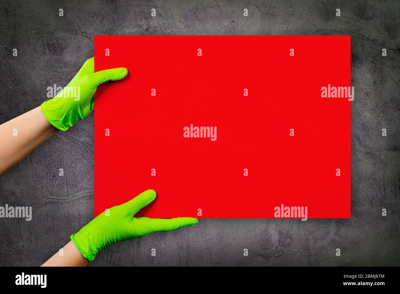Leere rote Karte in Arzthänden in grünen Handschuhen mit Kopierraum, auf grauer Zementmörtel-Wand. Stockfoto