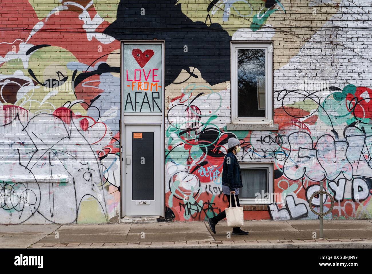 Toronto, Kanada, ein Mann mit Gesichtsmaske geht vor einer bunten Wand und zeigt während der Coronavirus-Pandemie eine positive soziale Distanzierung. Stockfoto