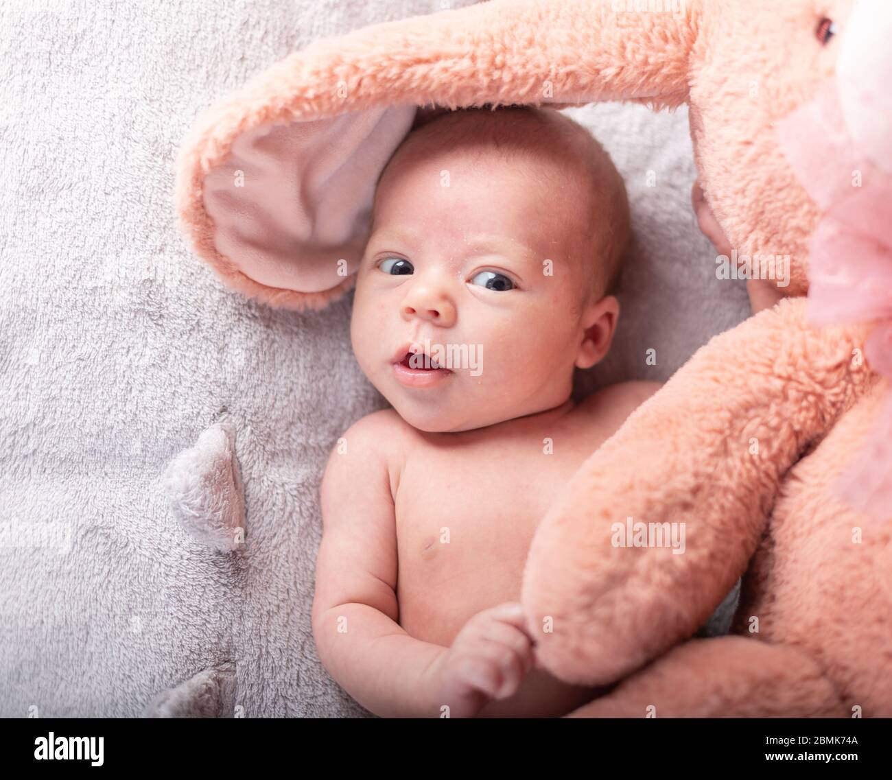 Ziemlich lächelndes Baby Mädchen und Spielzeug Kaninchen liegen in hellen Hintergrund Stockfoto