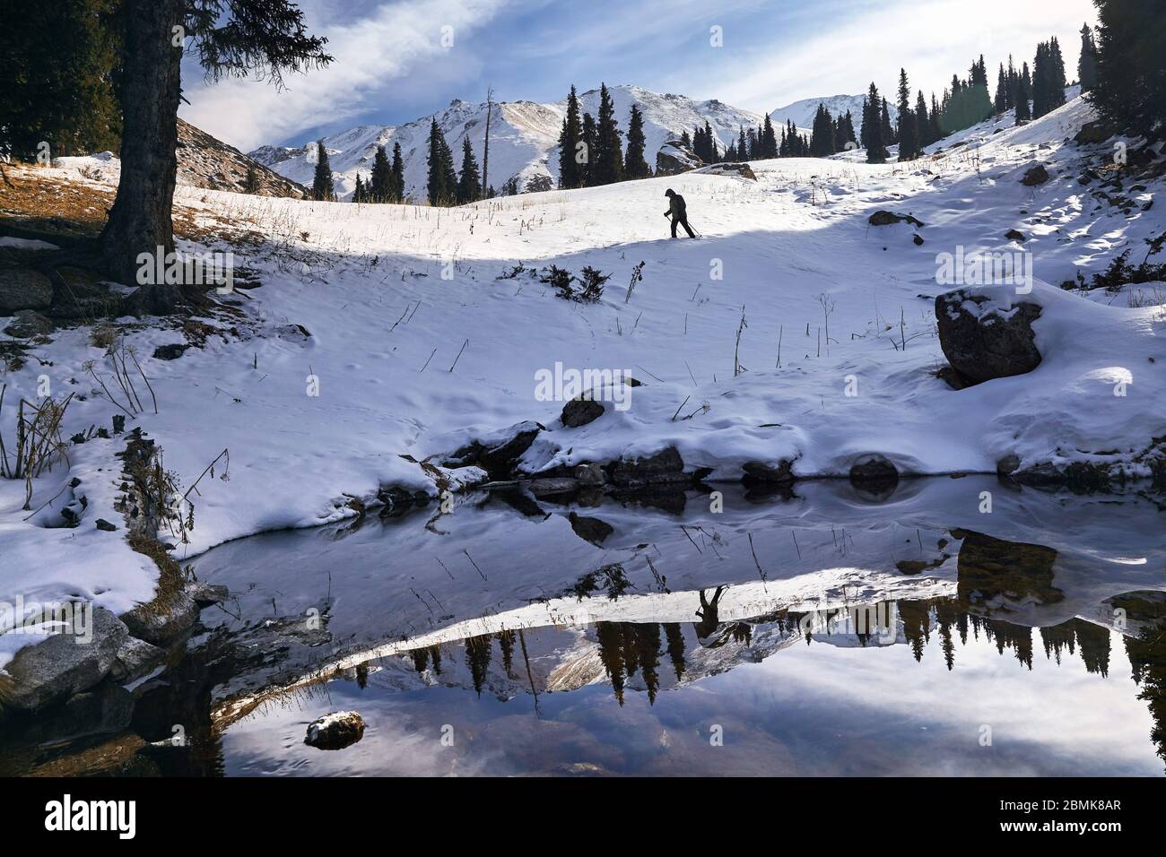 Einsamer Mann mit Trekking Pole zu Fuß den Hügel in der Nähe von See mit Reflexion an Winter in Kasachstan und Zentralasien Stockfoto
