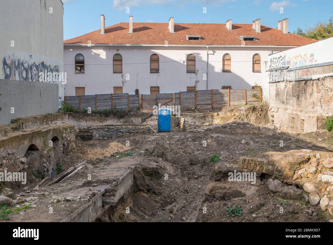 Ein tragbares Badezimmer befindet sich in der Mitte einer archäologischen Ausgrabungsstätte, die bald eine Baustelle in der Altstadt werden wird. In Vilnius, Litauen. Stockfoto