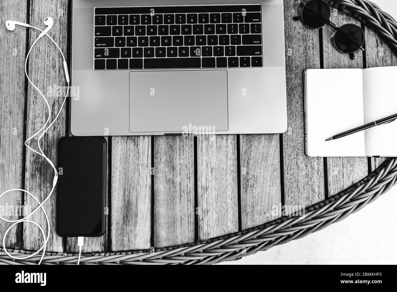 Schwarz-weiß Foto von oben eines Arbeitsbereichs mit Laptop, auf einem Holztisch mit Smartphone und einem Notebook für die Aufnahme von Koffern. Business con Stockfoto