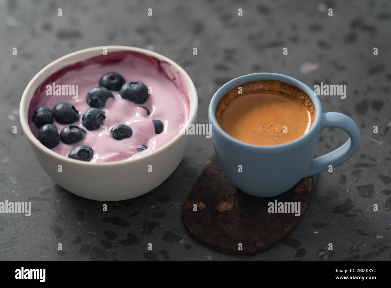 Heidelbeerjoghurt mit ganzen Beeren und einer Tasse frischen Espresso Auf konkretem Hintergrund Stockfoto