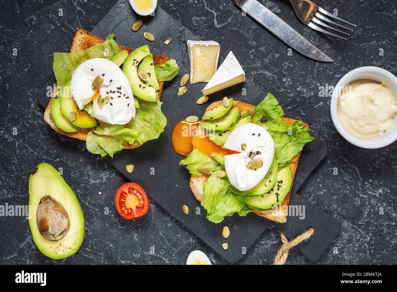 Gesundes Sandwich - pochierte Eier und Avocado auf Toast mit Tomaten auf blsck Stein Hintergrund. Draufsicht Stockfoto