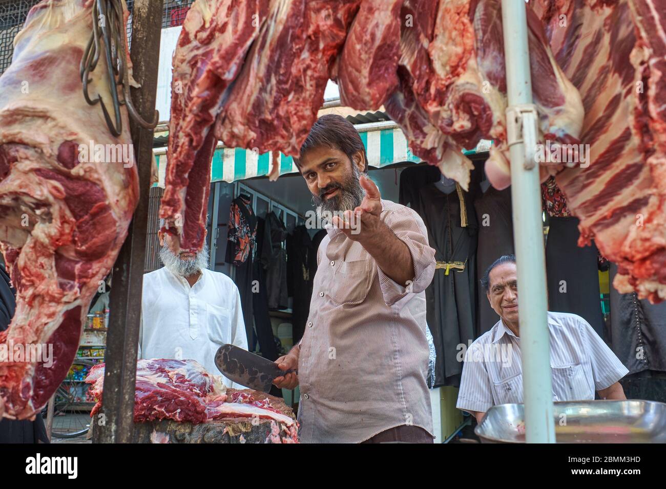 Ein muslimischer Metzger in Arab Gali, Grant Rd., Mumbai, Indien, umrahmt von großen Fleischstücken und einem breiten Stück Fleisch in der Hand, der den Fotografen aggressiv anstichtend Stockfoto