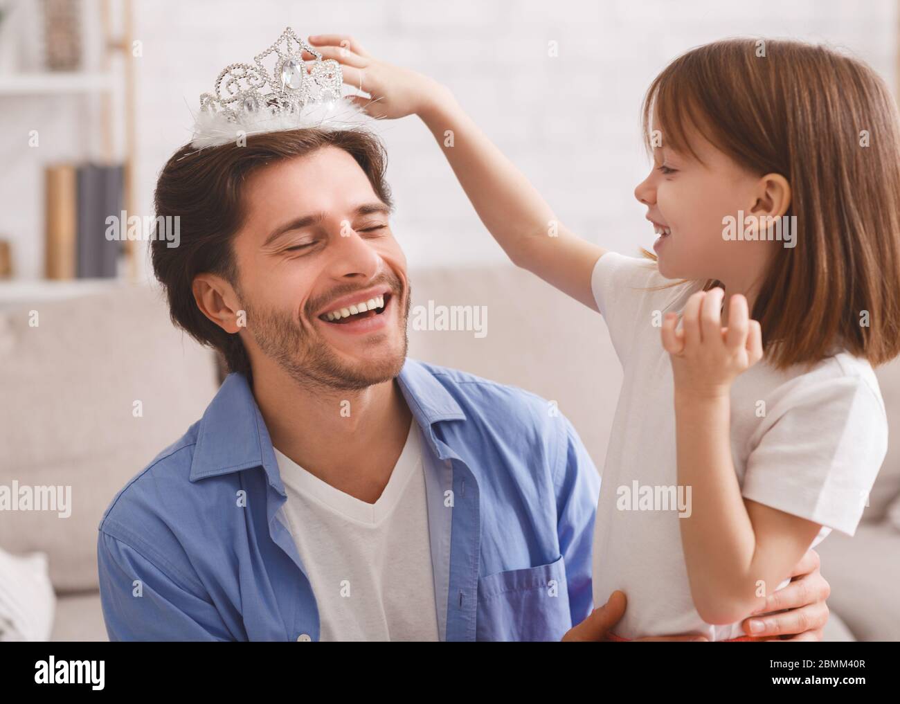 Kleines Mädchen, das Krone auf den Kopf ihres lachenden Vaters legt Stockfoto