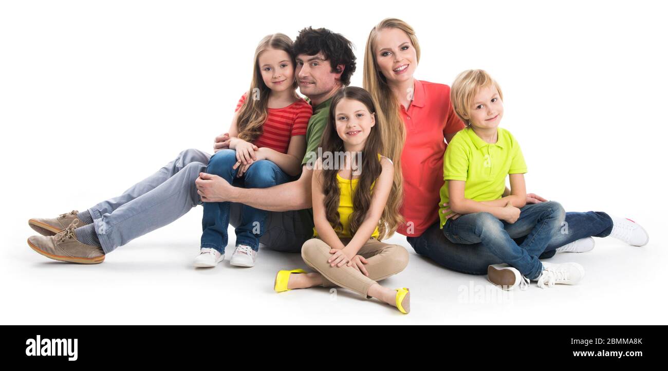 Glücklich lächelnde Familie von zwei Eltern und drei Kinder sitzen auf dem Boden Studio auf weißem Hintergrund Stockfoto