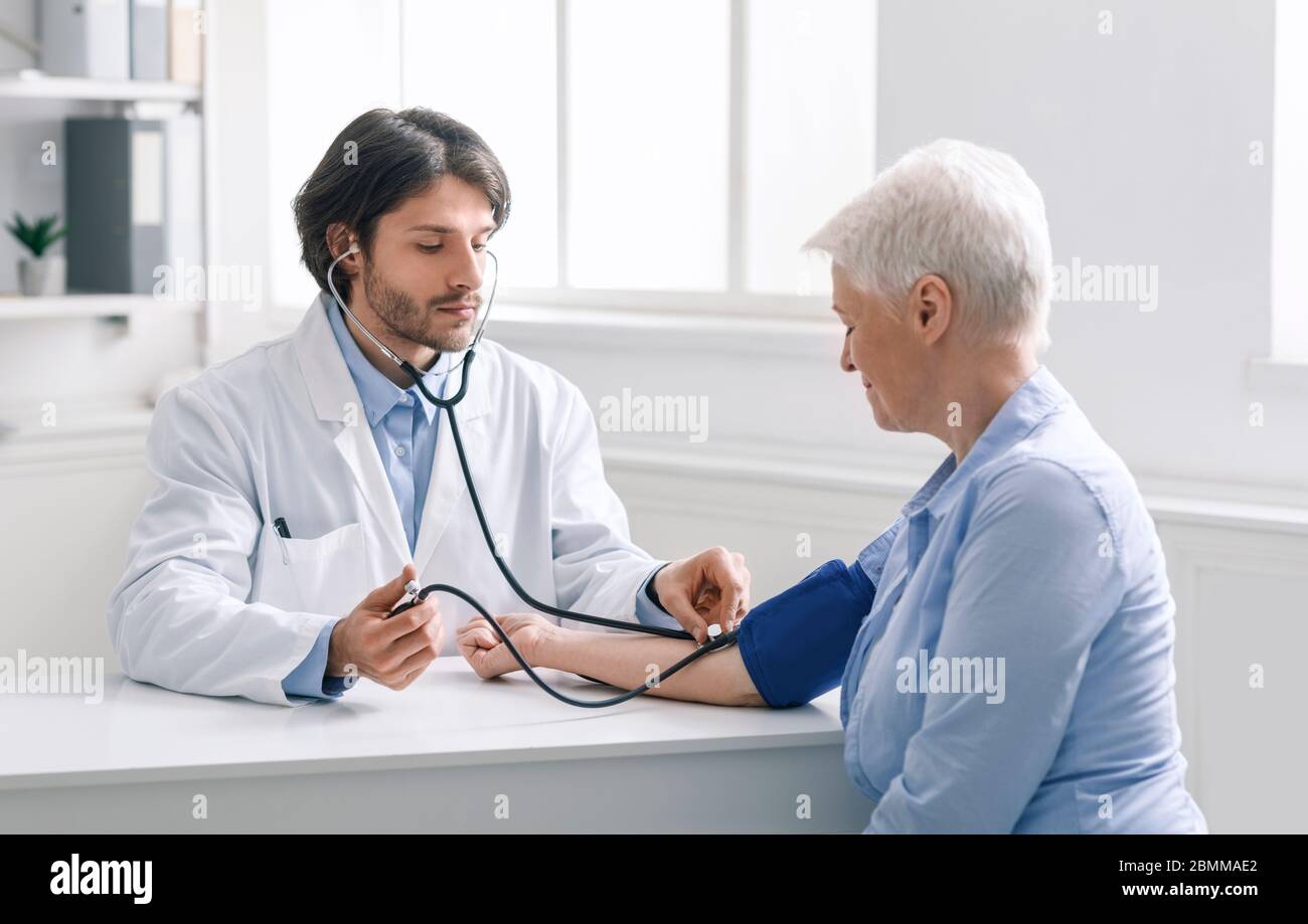 Junger Arzt, der den Blutdruck einer älteren Frau misst Stockfoto