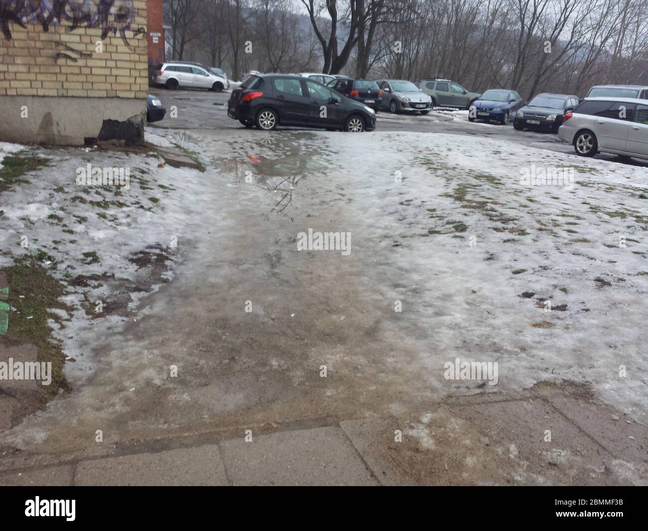 Fußgängerweg mit Schnee, Wasser und Schlamm bedeckt. Parkplatz im Hintergrund Stockfoto