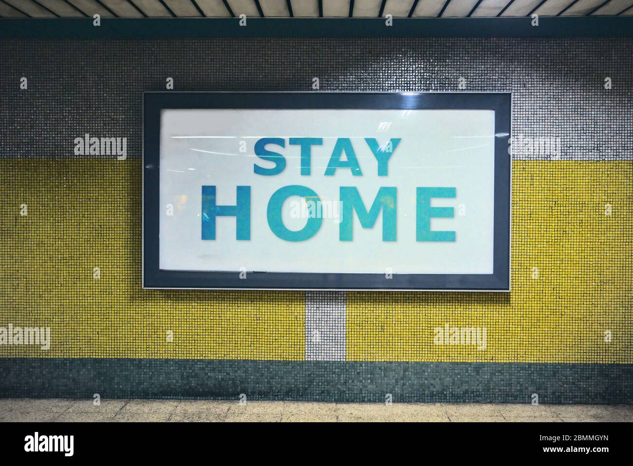 Die Aufmerksamkeit errichtende Plakatwand mit der Botschaft von zu Hause bleiben Anfrage, um Menschen sicher vor Coronavirus an einer Wand an U-Bahn-Korridoren platziert bleiben Stockfoto