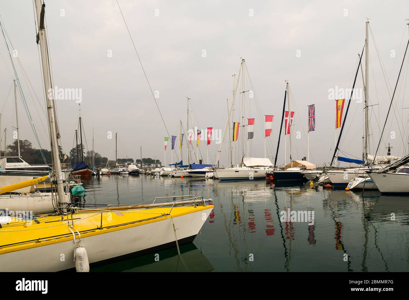 Blick auf den kleinen Hafen von Bardolino am Ufer des Gardasees mit vertäuten Segelbooten und Europafiggen an einem bewölkten Tag, Verona, Venetien, Italien Stockfoto