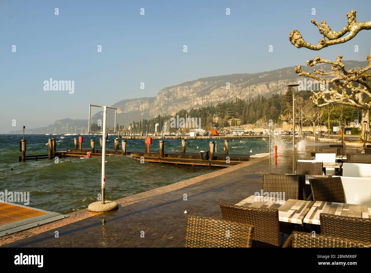 Panoramasicht auf die Seepromenade mit einem leeren Café im Freien an einem windigen Tag mit hohen Wellen, Garda, Verona, Veneto, Italien Stockfoto