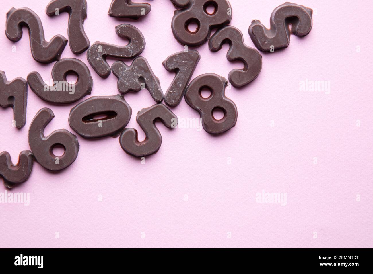 Ein kunstvoller Studiofoto mit Schokoladennummern vor einem pastellrosa Hintergrund Stockfoto
