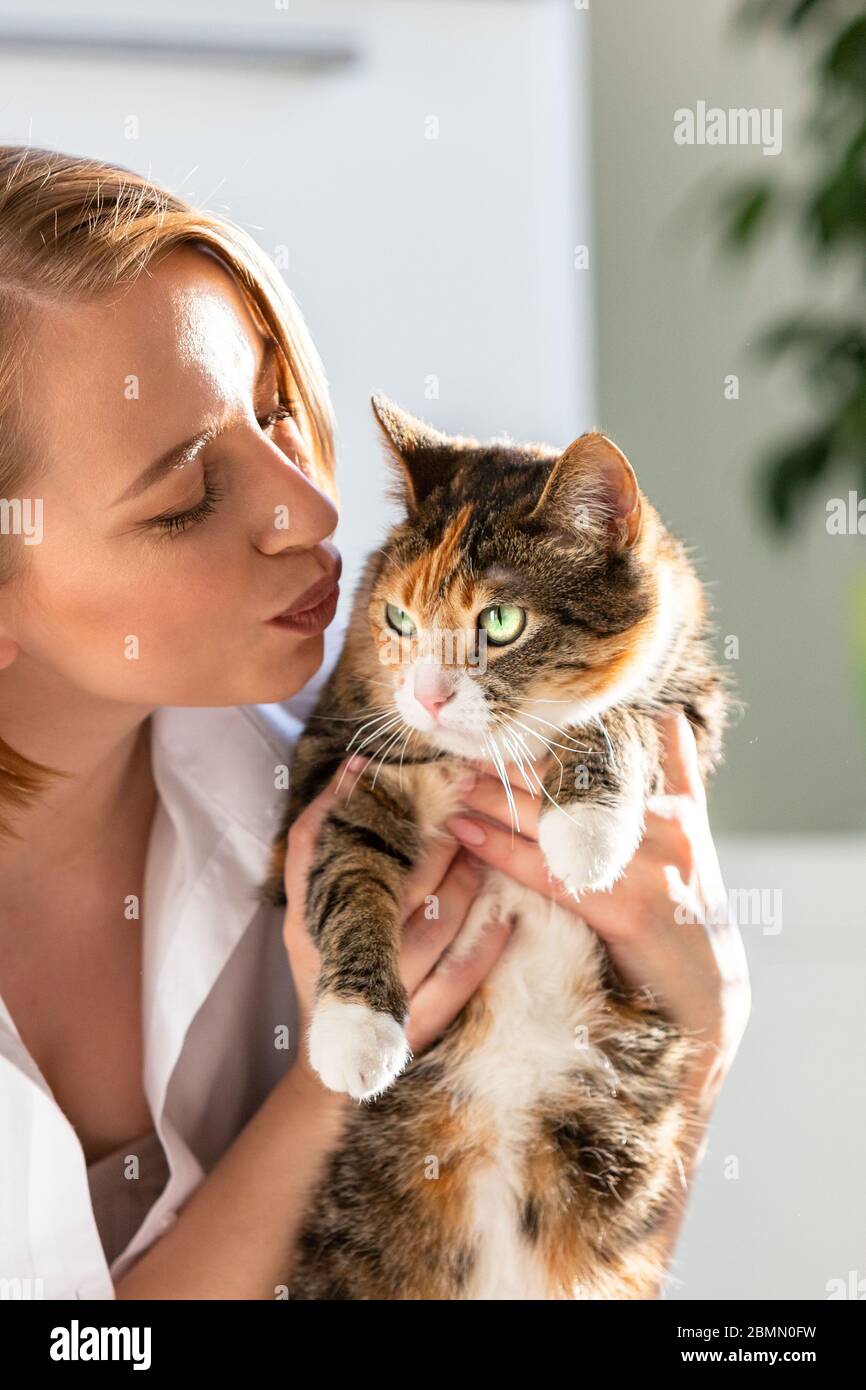 Nahaufnahme von lächelnden Frau in weißem Hemd küssen und umarmen mit Zärtlichkeit und Liebe Katze, halten sie in den Armen. Liebe zu den Tieren, Haustiere Konzept Stockfoto