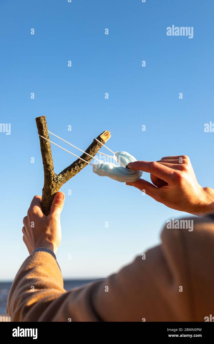 Der Mensch verwendet eine schützende medizinische Maske als Schleuder aus dem Ast, blauer Himmel auf Hintergrund, selektiver Fokus. Genießt das Leben, zurück zum normalen Leben nach CO Stockfoto