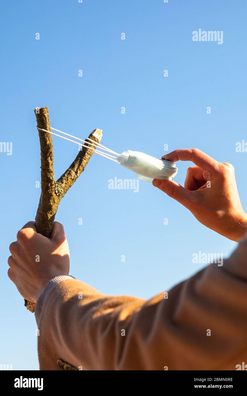 Der Mensch verwendet eine schützende medizinische Maske als Schleuder aus dem Ast, blauer Himmel auf Hintergrund, selektiver Fokus. Genießt das Leben, zurück zum normalen Leben nach CO Stockfoto