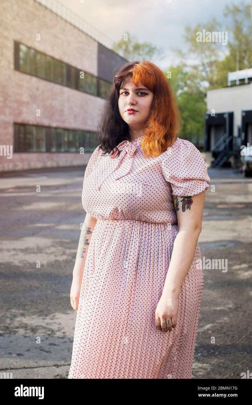 Moskau, Russland - 02. Mai 2020 , Street style. Ein junges Mädchen mit roten Haaren in einem rosa Seidenkleid mit einem Faltenrock posiert vor der Kulisse einer ur Stockfoto