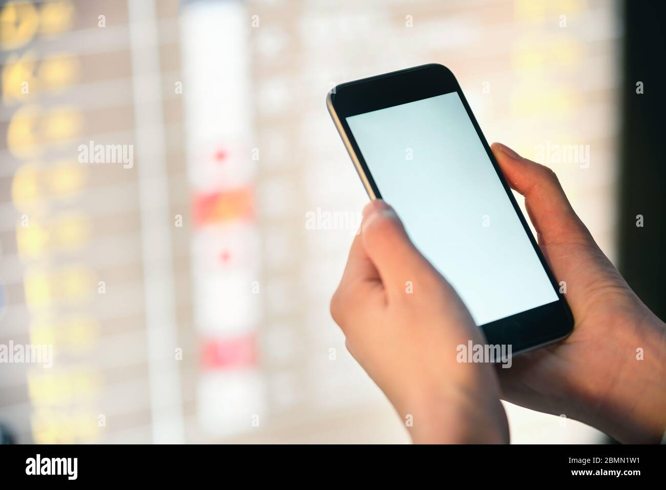 Mockup-Bild von weiblichen Händen halten schwarzen Handy mit leeren weißen Bildschirm über Bord im Flughafen-Terminal Stockfoto
