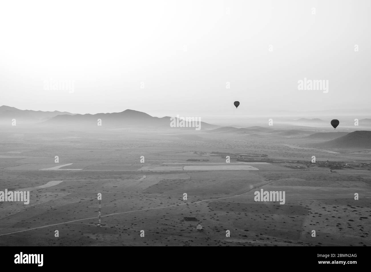 Schwarz-Weiß-Bild im Retro-Stil von einem Heißluftballon über Marokko. Zwei weitere Ballone in der Luft über einer wunderschönen Bergkette Stockfoto