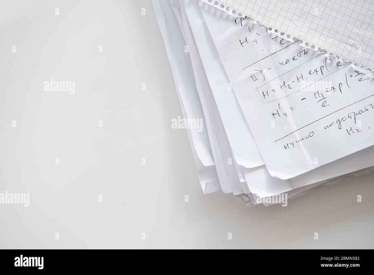 Stapel Papier mit handschriftlichen Aufzeichnungen wissenschaftlicher Formeln unter einem karierten Notizblock. Kopierbereich. Draufsicht. Stockfoto