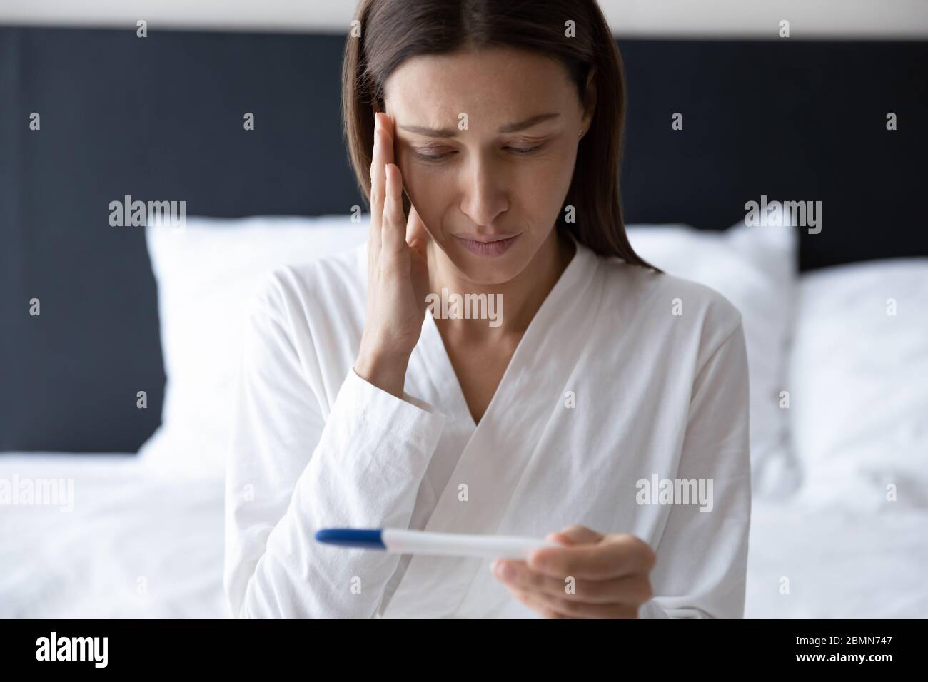 Frau, die Schwangerschaftstest betrachtet, fühlt sich besorgt über schlechte Nachrichten Stockfoto