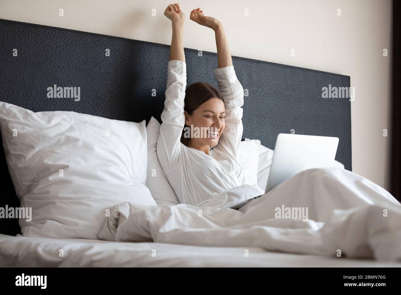 Erwachte Frau Stretching im Bett mit Laptop fühlt sich glücklich Stockfoto