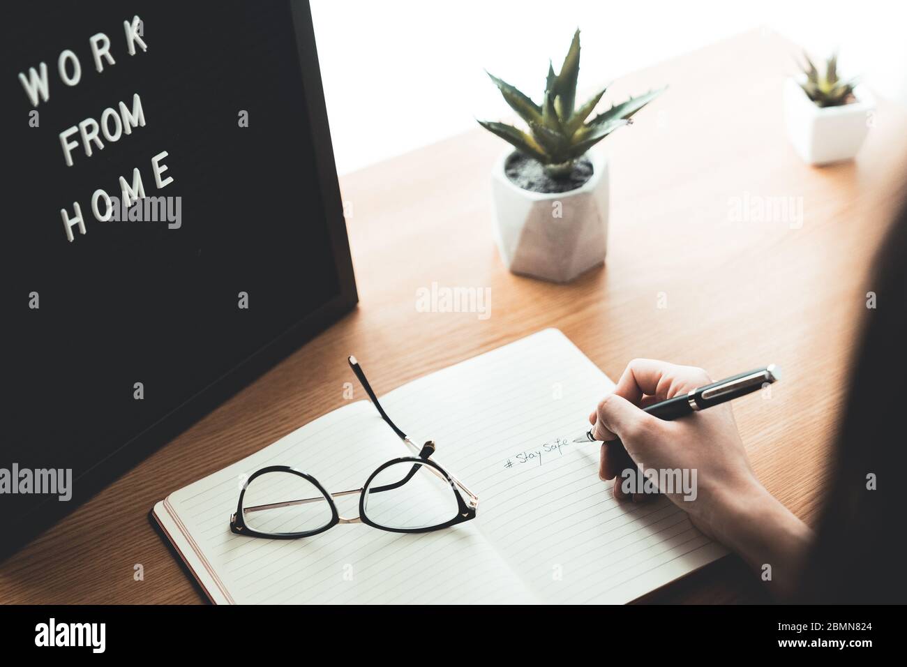 Rückansicht der Frau Hand mit Bleistift Schreiben Bleiben Sie sicher auf dem Notebook am Schreibtisch zu Hause. Arbeit von zu Hause und Quarantäne-Konzept auf Epidemien Ausbruch. Stockfoto
