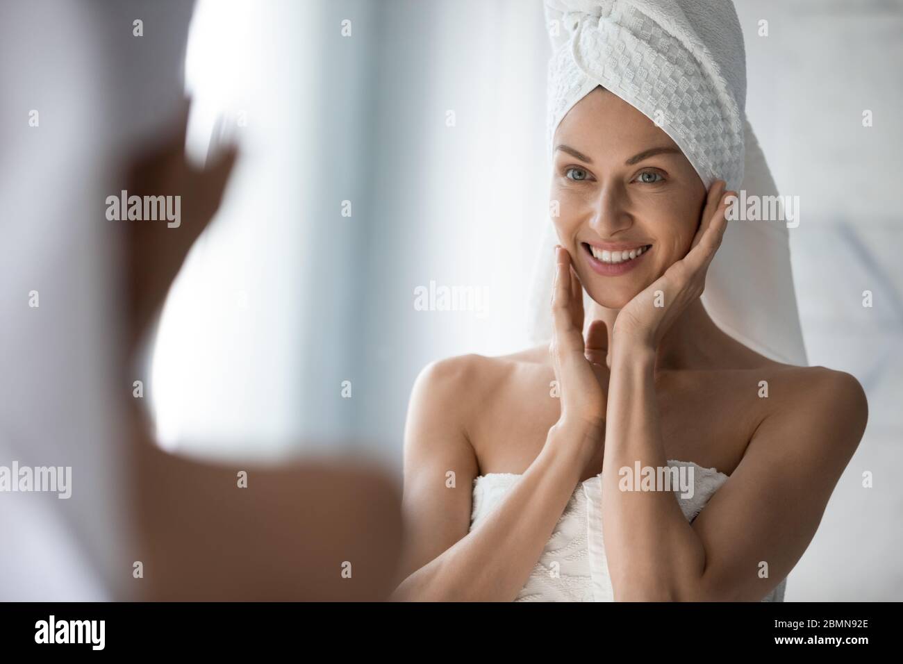 Frau sieht in Spiegel berührt mit Feuchtigkeit versorgt gesunde Haut fühlt sich zufrieden Stockfoto