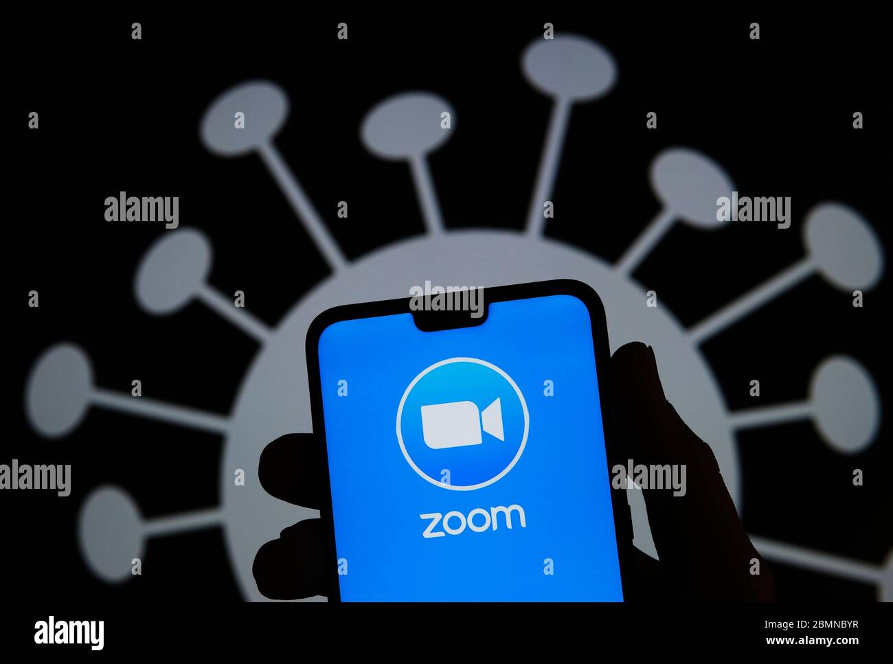 Stone / Großbritannien - Mai 10 2020: Zoom App Logo auf Smartphone Silhouette in der Hand halten. Coronavirus-Bild auf dem verschwommenen Hintergrund. Echtes Foto, Stockfoto