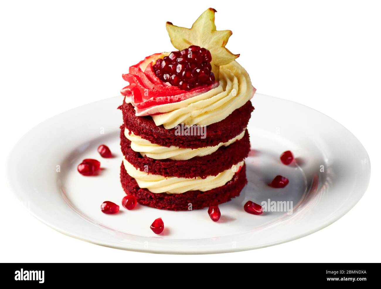 Köstliche Kuchen Red Velvet mit Schlagsahne, Granatapfel und Karambola auf weißem Teller dekoriert, serviert mit einem Glas Früchtetee. Isoliert über Weiß Stockfoto