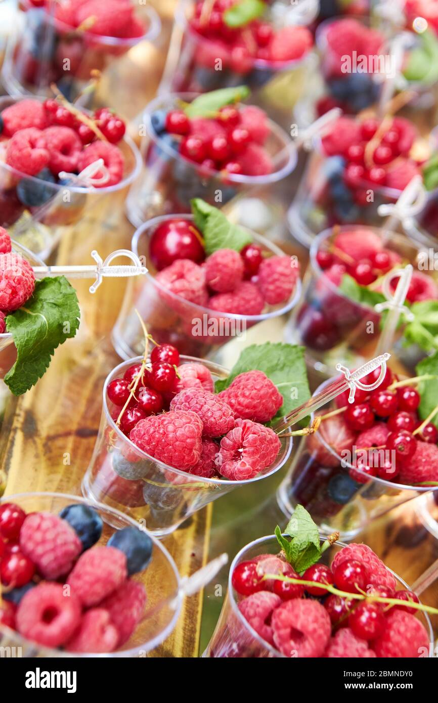 Frische Beeren in Plastikbechern zum Verkauf oder Buffet auf Holztisch angeordnet. Stockfoto