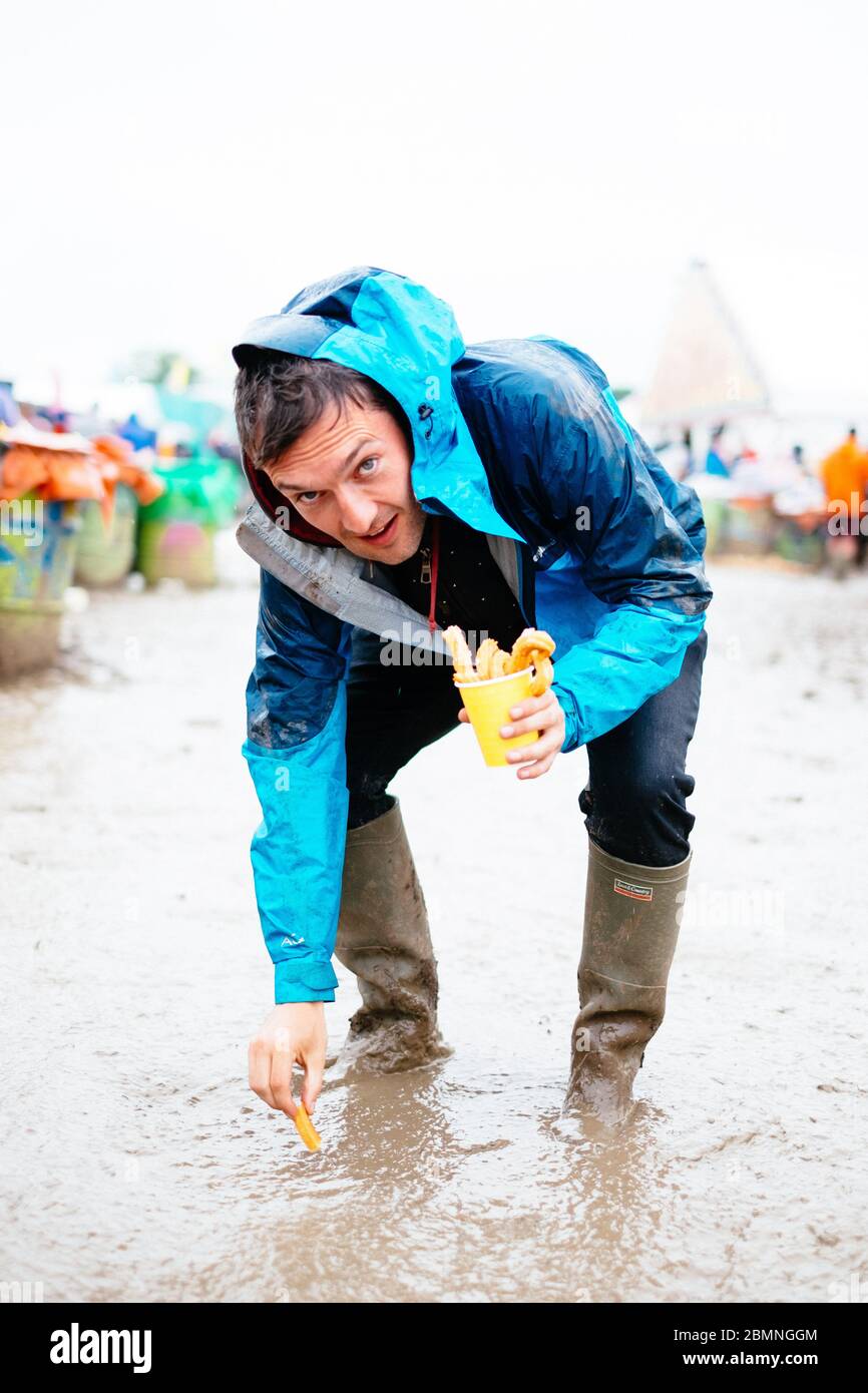 Ein Mann, der vorgibt, Choros in den Schlamm zu tauchen, Regenmantel und wellington-Stiefel trägt Glastonbury Festival 2016 – Bilddatum Sonntag, 26. Juni 2016 (Pi Stockfoto
