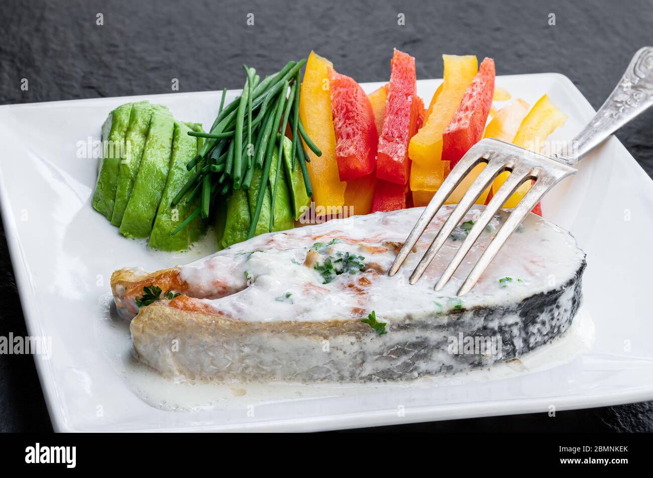 Lachssteak mit cremiger Sauce und gemischtem Gemüse auf schwarzem Steingrund Stockfoto